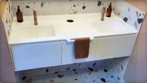 Plan vasque monobloc sur mesure avec double vasque, porte-serviette intégré et orifice d’accès à la poubelle, tiroirs fermés.